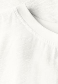 Tissu en coton blanc de t-shirt avec un col rond à côtes et une texture lisse. Un léger détail de surface froissée est visible.