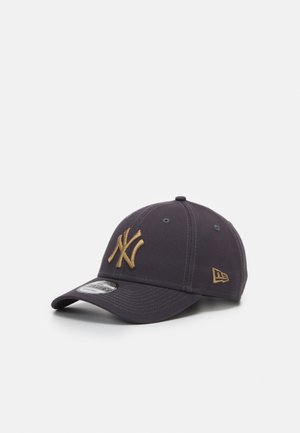 Casquette de baseball gris foncé avec le logo doré des New York Yankees sur le devant et un petit logo doré New Era sur le côté, posée sur une surface blanche.