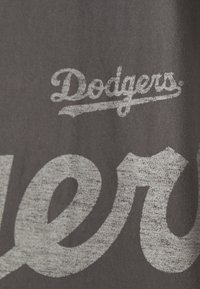 Svart tygtröja med vit sliten text som läser "Dodgers" i kursiv stil, med fet stil och en vintage-look.