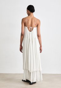 Weißes Maxikleid mit vertikalen Streifen, tiefem Rückeneingang, Spaghetti-Trägern und mehrlagigem Rock; aus leichtem, fließendem Stoff gefertigt.