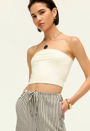 Biały strapless crop top w połączeniu z szarymi i białymi, luźnymi spodniami w paski. Dodatki obejmują warstwowy złoty naszyjnik i bransoletkę.