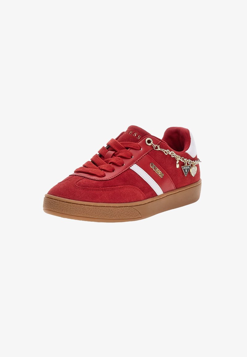Sneaker in suede rosso con striscia bianca, suola marrone, lacci rossi, loghi dorati "GUESS" e catena di charm dorati pendente sul lato.