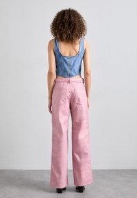 Kort denimtop med tjocka axelremmar och dragkedja i ryggen, ihop med högmidjade, vida rosa byxor med bakfickor och slät textur.