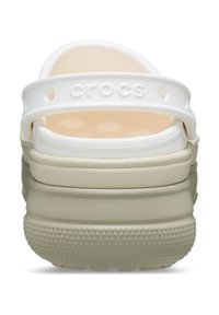 Zoccoli bianchi con suola piatta beige, dotati di cinturino posteriore, superficie liscia e fori di ventilazione rotondi. Logo impresso sul tallone.