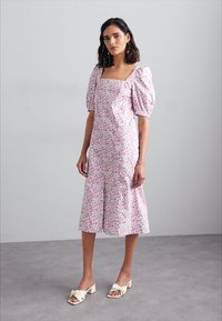 Cvečno midi obleko v roza barvi s puhastimi rokavi in kvadratnim izrezom. Izdelana je iz lahkotnega blaga, ima razširjen rob in subtilen cvetlični vzorec.