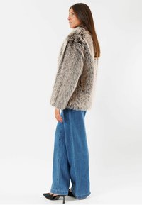 Cappotto in pelliccia sintetica nelle tonalità di grigio e beige, con una vestibilità comoda, maniche lunghe e una texture morbida, abbinato a jeans a gamba larga e tacchi appuntiti.