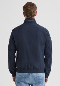 Marineblaue Bomberjacke aus leichtem Material, mit geripptem Saum und Bündchen sowie einem kleinen Logotag auf der Rückseite des Kragens.