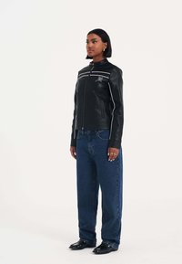 Svart läderjacka med vita ränder, hög krage och framzipper. Bärs med löst sittande blå denimjeans och svarta skor.