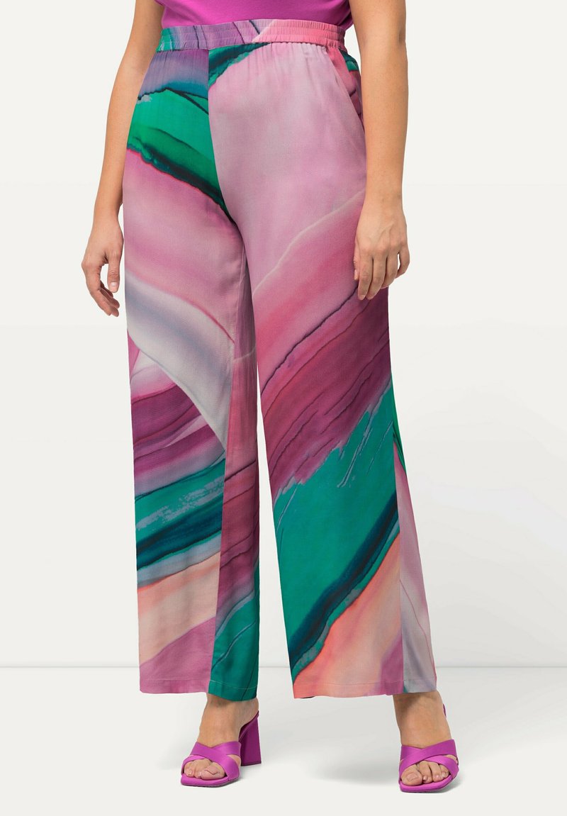 Videbenede bukser med et farverigt abstrakt print i pink, grøn og lilla, båret med lilla hæl-sandaler.