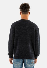 Maglione lavorato a maglia blu scuro con scollo rotondo e polsini a coste, caratterizzato da una finitura testurizzata e una vestibilità comoda, abbinato a jeans azzurri chiari.