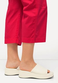 Gräddfärgade öppna plattformssandaler med en slät yta och ett brett rem, i kombination med korta röda byxor som visar anklarna och fötterna.