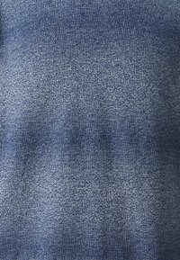 Denimsko stoff i en mellomblå nyanse, med en teksturert overflate som har en lett glans og subtile variasjoner i farge og mønster.