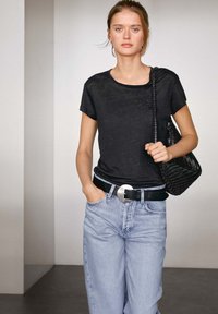 Zwarte T-shirt met korte mouwen, gemaakt van een gestructureerde stof, gecombineerd met hoogstaande lichtblauwe denim jeans en een brede zwarte riem met een ronde gesp.