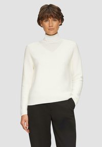 Witte v-hals trui met een getailleerd ontwerp, geribbelde textuur en lange mouwen, gecombineerd met zwarte broek. Zachte, lichtgewicht stof.