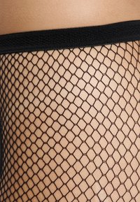 Collant in rete nera con motivo a diamante, dotati di un elastico in vita morbido e di una texture trasparente, posizionati su uno sfondo di tono pelle.