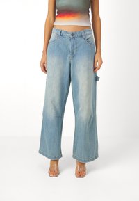 Světle modré denimové kalhoty s širokými nohavicemi a bledým povrchem, předními kapsami a detaily kapsy na boku. Obsahují zapínání na knoflík a poutka na opasek.