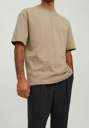 Beżowy bawełniany t-shirt z krótkim rękawem, okrągłym dekoltem, luźnym krojem i minimalistycznym wzornictwem, noszony z ciemnymi spodniami.