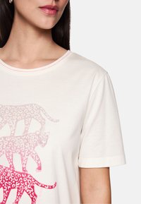 Beige Baumwoll-T-Shirt mit rundem Ausschnitt, das ein Farbverlauf-Leopardenmuster in Rosatönen aufweist. Kurze Ärmel und gestickte Akzente.