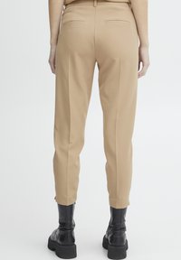 Beige op maat gemaakte broeken met een rechte snit, voorzien van achterzakken en een gladde textuur. Gecombineerd met zwarte rits-enkelboots.