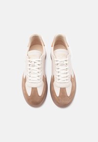 Μπεζ και ανοιχτό καφέ σουέντ αθλητικά παπούτσια με λευκά κορδόνια, στρογγυλές μύτες και καστανοκίτρινες λεπτομέρειες, σε λήψη από ψηλά πάνω σε λευκό φόντο.