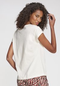 Cremfarbene Baumwoll-T-Shirt mit kurzen Ärmeln und lässiger Passform, mit einem runden Ausschnitt. Ausgestellt mit gemusterten Hosen.