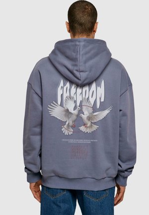 Grau Kapuzenpullover aus oversized Stoff. Mit einem zentralen Grafik von Tauben und dem Wort "FREIHEIT" in stilisiertem weißen Text.