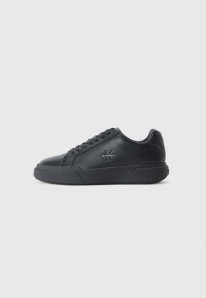 Black leather sneakers feature a rounded toe, flat sole, and lace-up design. Notable details include a subtle logo on the side.