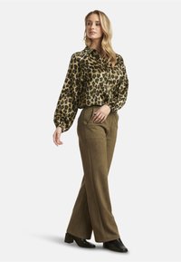 Leopard print blouse with puffed sleeves, paired with high-waisted olive green trousers and black ankle boots. Smooth fabric, relaxed fit.