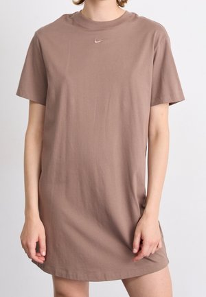 Personne portant une robe t-shirt Nike ample à manches courtes de couleur marron, avec un petit logo Swoosh centré près de l'encolure.