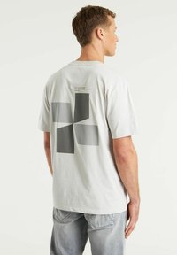 Camiseta de algodón gris claro con un gran gráfico abstracto en gris oscuro en la parte trasera. Mangas cortas y corte relajado.