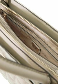 Sac à main matelassé beige avec plusieurs compartiments zippés ; doté de ferrures dorées et d'une doublure intérieure à motif.