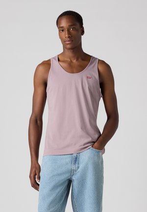 Top en coton lavande avec un col rond, présentant un petit logo rouge. Porté avec un jean en denim bleu clair, affichant une coupe décontractée.