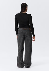 Haut noir à manches longues au design ajusté, associé à un jean en denim gris délavé, ample et doté d'un style classique à cinq poches et d'une finition texturée.