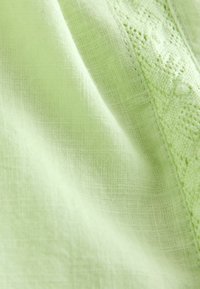 Világoszöld szövet texturált, szőtt mintával és varrott, díszített csipke szegéllyel az él mentén.