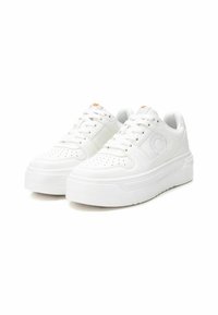 Zapatillas blancas de cuero suave con detalles perforados, cordones planos y una suela de goma gruesa. Incluye un acento naranja en la lengüeta.