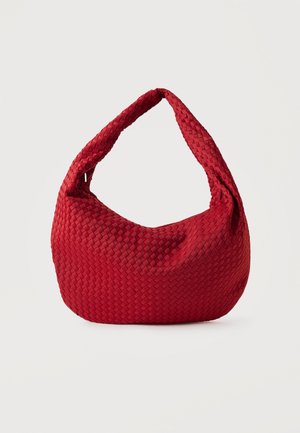 Bolso bandolera de cuero rojo trenzado con una sola correa ancha y una forma suave y redondeada sobre un fondo liso.