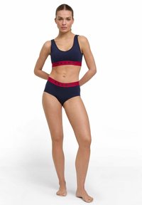 Set di reggiseno sportivo blu navy e slip a vita alta con bande elastiche rosse e logo "FALKE", realizzato in tessuto elastico e liscio.