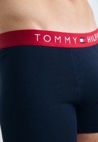 Boxeri scurți din bumbac bleumarin cu un tiv elastic roșu pe care este inscripționat logo-ul "TOMMY HILFIGER" în alb, textură netedă, design ajustat.