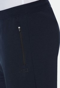 Marineblaue Sporthosen aus weichem Stoff, mit einer seitlichen Reißverschlusstasche und einem dezenten Logo in einer kontrastierenden Farbe.