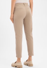 Beige cotton trousers with a fitted waist, tapered leg, and two back pockets. Features a subtle texture and a hemmed cuff at the ankle.
