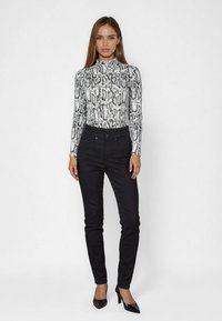 Black jeans paired with a high-neck, long-sleeve bodysuit featuring a white and black snake print pattern. Model wearing black heels.