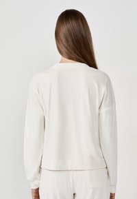 Felpa leggera color crema con scollatura a girocollo, maniche lunghe e vestibilità rilassata. Tessuto morbido, dettagli con polsini e vita a costine.