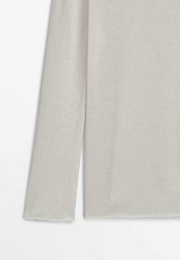 Pull en maille beige clair avec une finition texturée, doté d'un col rond et de manches longues, présentant une coupe légèrement ample et un ourlet effiloché.