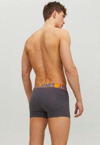 Graue Boxer-Briefs mit einem orangefarbenen Bund, auf dem "JACK & JONES" in Blau steht. Der Stoff wirkt weich und glatt. Mittlere Oberschenkellänge.