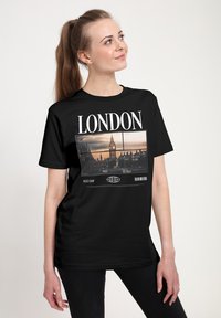 Černé tričko s fotografickým potiskem Londýnského Big Bena a bílým textem "LONDON" a "NEXT STOP". Pohodlný střih s krátkými rukávy.