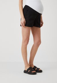 Sorte shorts med avslappet passform, elastisk midje og side lommer. Kombinert med kraftige svarte sandaler. Glatt stoff, uformell design.
