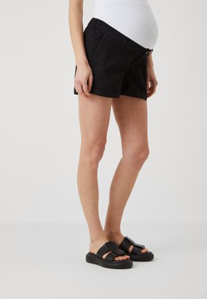 Black shorts with a relaxed fit, elastic waistband, and side pockets. Paired with chunky black slide sandals. Smooth fabric, casual design.
