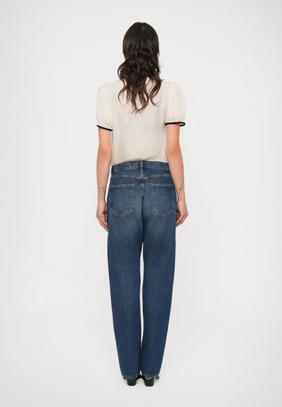 Ανοιχτόχρωμη, υφασμάτινη μπλούζα με φουσκωτά μανίκια και μαύρο περίγραμμα, σε συνδυασμό με ψηλόμεσα, φαρδιά σκούρα μπλε τζιν με πίσω τσέπες.