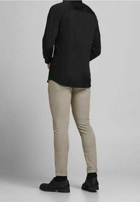 Svart långärmad skjorta, slim-fit beige rutiga byxor och svarta skor. Slät tyg med en subtil lyster på skjortan.