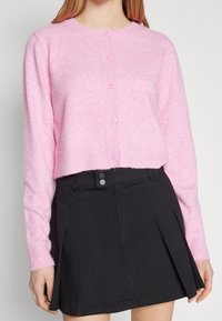 Rosa stickad kofta med rund hals och sex knappar framtill. Texturen är mjuk och fluffig. Matchad med en svart kjol.